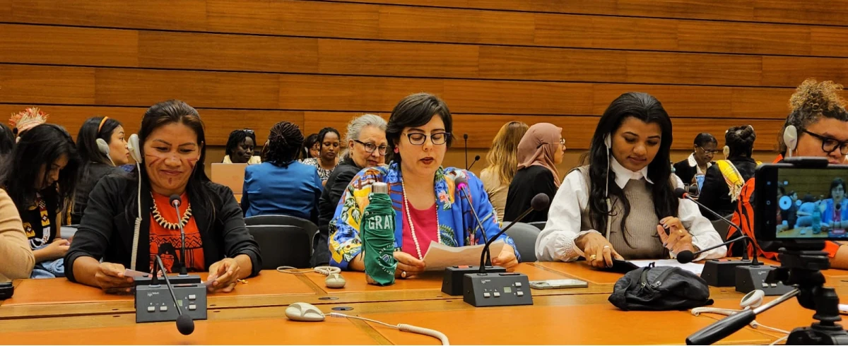 Three women talking (Tamara in the middle) and taking notes at a conference panel, with a camera recording in the foreground.