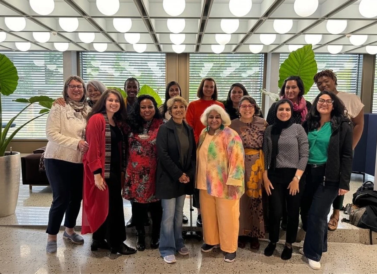 A group of women posing together in a well-lit room with plants.