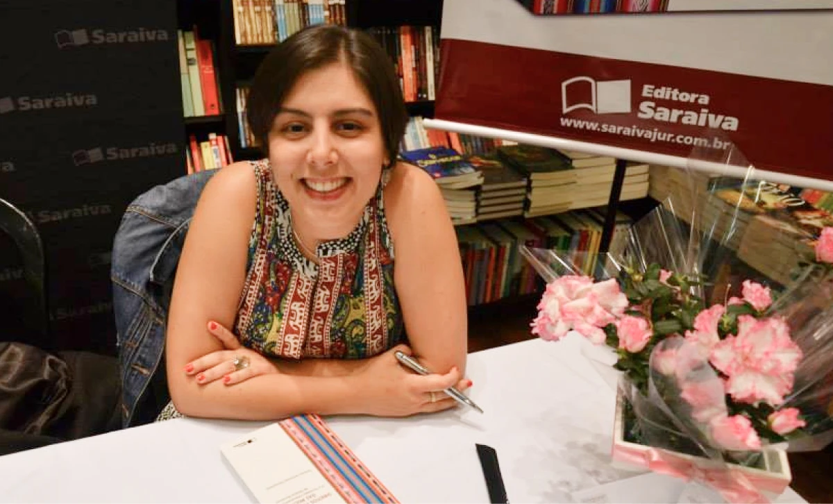 Tamara Gonsalves smiling while signing a book at a table with flowers and books.